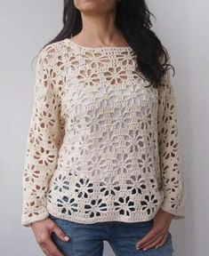 a woman standing in front of a white wall with her hands on her hips, wearing jeans and a crocheted sweater