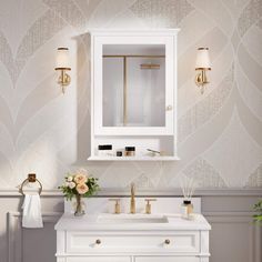 a white bathroom vanity with gold fixtures and flowers on the counter top, in front of a wall - mounted mirror