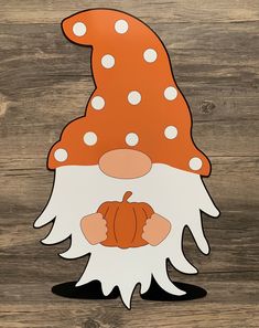 an orange and white gnome's head with polka dots on the top, sitting on a wooden surface