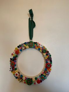 a wreath made out of buttons hanging on the wall with a green ribbon around it