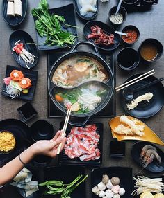 a table topped with black bowls filled with food and chopsticks on top of it