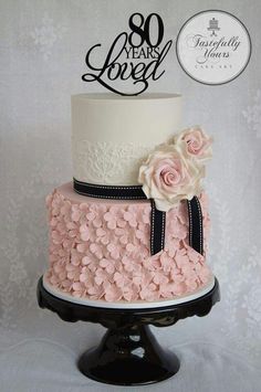 a three tiered cake with pink flowers on top and black ribbon around the edges