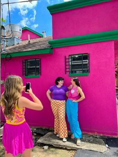 three women standing in front of a pink house