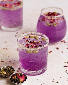 two glasses filled with purple liquid next to some dried flowers and spices on the table