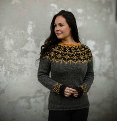 a woman standing in front of a wall wearing a sweater with an intricate design on it