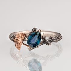 "A hand-made twig and Ginkgo leaf ring set with a pear-shaped teal sapphire. The ring displays a beautiful twig pattern along with a Ginkgo leaf that creates a pleasantly asymmetrical result. A delicate, handmade engagement ring made in two gold colors and set with a natural, high-quality sapphire. The grooves in the band are plated with black rhodium which emphasizes the texture. if you prefer not to apply the black rhodium that is fine. The center stone is a 5mmX7mm natural teal sapphire of high quality. Please note that the sapphires are natural stones and the exact shade may vary. If you are looking at this ring then you are probably looking for something special, something different. The engagement rings I design are made of 100% recycled gold and non-conflict diamonds in high quality Handmade Engagement Ring, Twig Engagement Ring, Green Sapphire Ring, Saphir Ring, Leaf Engagement Ring, Teal Sapphire, Handmade Engagement Rings, Ginkgo Leaf, Ring Displays