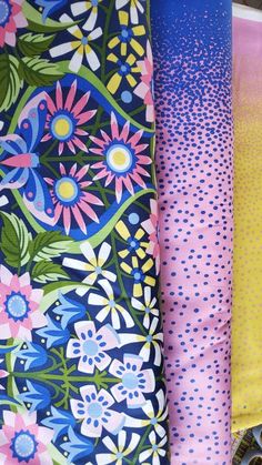 three different colored fabrics are lined up on a tablecloth covered with polka dots and flowers