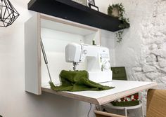 a sewing machine sitting on top of a white table next to a green blanket and chair