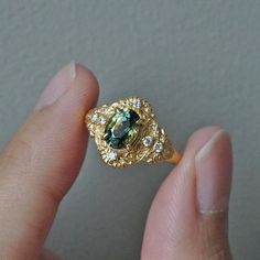 a close up of a person's hand holding a ring with a green stone