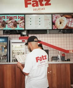 a man standing in front of a donut shop holding a doughnuts menu