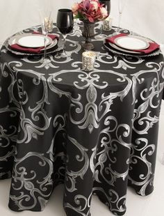 a black and white table cloth with silver swirls on it is set for two