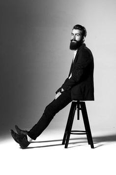 a man sitting on top of a wooden stool next to a white wall in black and white