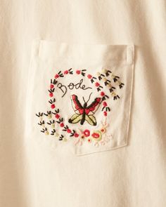 a white shirt with embroidered words and a butterfly on the chest pocket that says bood