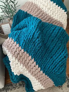 a blue and white knitted blanket sitting on top of a wooden table next to a potted plant