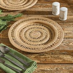 two woven placemats on a wooden table with spoons and napkins next to them