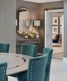 a dining room table with blue chairs and a round mirror on the wall above it