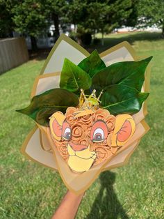 a person holding up a paper mask with leaves on it's head in the grass