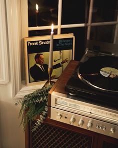 a record player sitting on top of a table next to a window with a candle