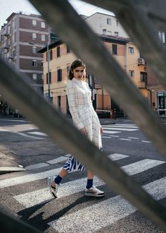 a woman walking across a street next to tall buildings