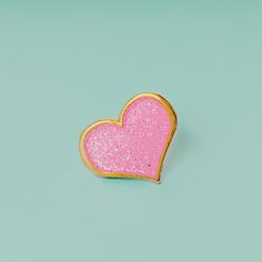 a pink heart shaped brooch sitting on top of a blue surface with gold trim