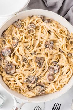 a pan filled with pasta and mushrooms on top of a white table next to silverware