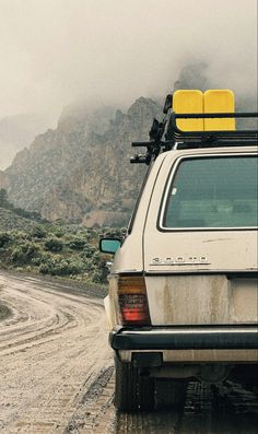 the back end of a white car on a dirt road with mountains in the background