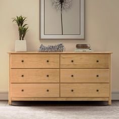 a wooden dresser sitting in front of a painting and potted plant on top of it