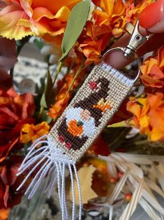 a hand holding a beaded keychain in front of flowers