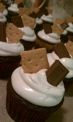 chocolate cupcakes with white frosting and crackers on top, sitting on a table