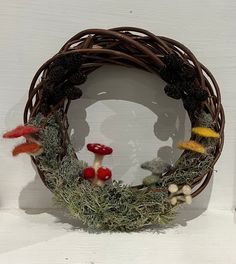 a wreath with mushrooms, moss and pinecones on the front is displayed against a white wall