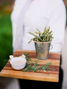 a person holding a wooden tray with a potted plant on it and sauce in front of them