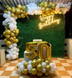 a 50th birthday party with balloons and gold foil numbers in front of a green wall