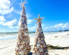 two christmas trees made out of seashells and starfish are on the beach