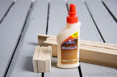 a bottle of wood glue sitting next to a wooden block on the ground with two pieces of wood in front of it