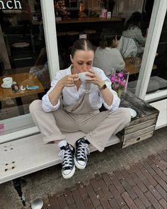 a woman sitting on a window sill drinking from a cup