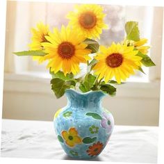 sunflowers are in a blue vase with green leaves on a white tablecloth