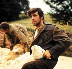 a man sitting on the ground with two sheep in front of him and another animal behind him