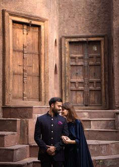 a man and woman standing next to each other in front of some wooden steps with their arms around each other