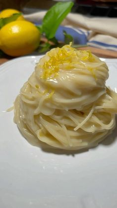 a white plate topped with pasta covered in sauce and lemon zest next to a green leafy plant