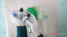 a person in white gloves holding a green and black cup with some paint on it