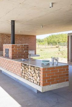 an outdoor kitchen with wood stacked on the counter and brick oven in the back ground