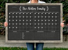 a woman holding up a chalkboard with the calendar for the kitchen family on it