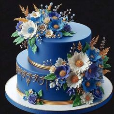 a three tiered blue cake with flowers on the top and gold trimmings