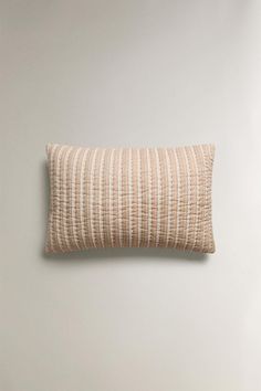 a beige and white striped pillow sitting on top of a wooden floor next to a wall