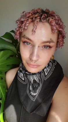 a woman with pink hair and piercings on her nose wearing a bandana, looking at the camera