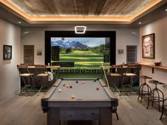 a game room with a pool table, bar stools and television on the wall