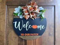 a welcome to our patch sign hanging on the front door with flowers and leaves around it