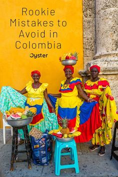 three women in brightly colored dresses sit on stools near a yellow wall with the words rookie misstakes to avoid in colombia