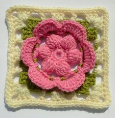 a crocheted square with a pink flower on it's center and green leaves