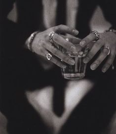 a person holding a glass with something in it's hand and wearing rings on their fingers